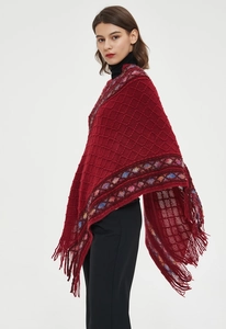 Detail of red knit poncho featuring diamond pattern and decorative fringe tassels