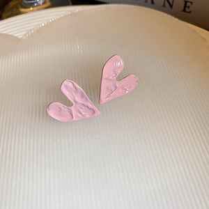 Close-up of pink heart stud earrings with unique hammered texture on white tray
