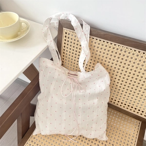 White canvas tote bag with pink heart patterns resting on a vintage rattan chair