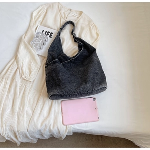 Detail view of large capacity black denim shoulder bag styled with a white dress and magazine