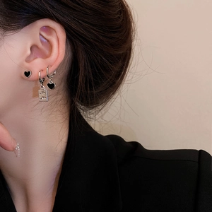 Close-up of black heart studs and rectangular relief pendant earrings on female model