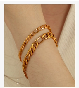 Detail of layered gold Figaro and Cuban link bracelets worn on a wrist with knit fabric