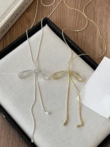 Detail view of gold and silver bow necklaces with droplet pendants on a linen display tray
