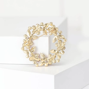 Macro shot of gold wreath brooch with rhinestones on a white geometric display stand