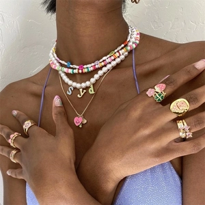 Layered gold necklaces with pearls, enamel letter charms and matching rings on model