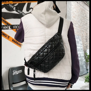 Detail of black quilted puffer waist bag with woven zipper pull worn as a crossbody