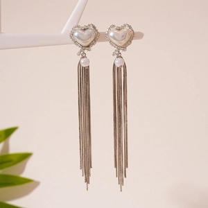 Detail of elegant heart-shaped pearl earrings with long silver snake chain tassels