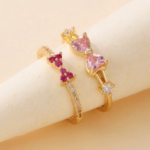 Elegante Goldringe mit rosa und roten herzförmigen Zirkonbögen auf beige Hintergrund