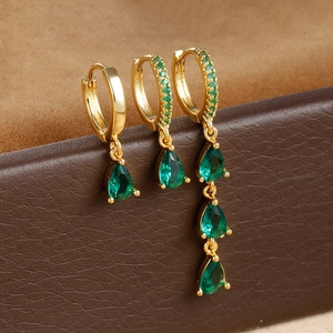 Macro shot of three-piece gold drop earrings with green zircons on leather display