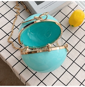 Close-up of a teal spherical hardshell bag with gold metal frame on a checkered cloth