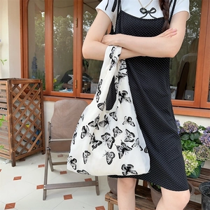 Detailed view of white canvas tote bag with black butterfly prints styled on a model