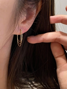 Detail of three-layer gold metal tassel earrings worn by a model in a side-view close-up