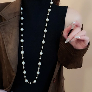 Detail showing long layered pearl necklace with golden chain on a black turtleneck sweater