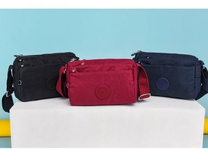 Three nylon crossbody bags in black, red, and navy blue displayed on a platform