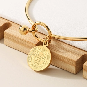 Detail shot of golden stainless steel St. Benedict medal charm on an open bangle