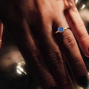 Detailed close-up of a gold-plated ring with blue pave setting worn on a finger