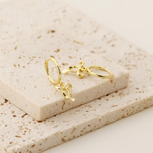 Detailed close-up of golden ribbon bow earrings on a beige textured stone background