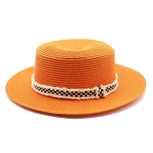 Détail d'un chapeau de paille orange avec ruban à damier effiloché et tissage texturé