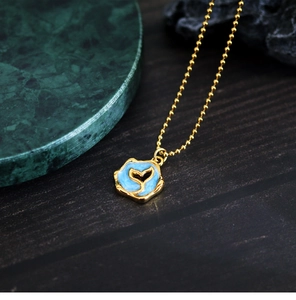 Macro shot of gold fishtail necklace with blue enamel pendant on marble texture