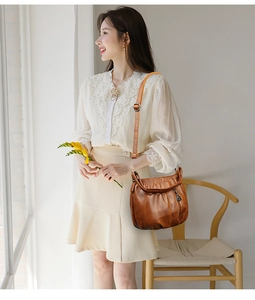 Close-up of brown pleated crossbody bag showing leather texture and gold metal buckle detail