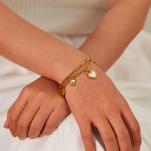 Detail of double-layer gold heart bracelet worn by model on soft white fabric