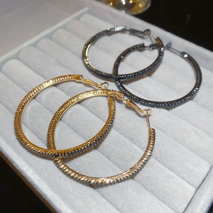 Detail view of gold and gunblack hoop earrings with dark zircons on a velvet display