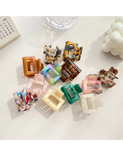 Detail showing a colorful assortment of small acetate claw clips on white textured leather