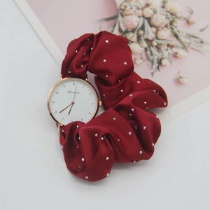 Detail of rose gold watch face with burgundy satin scrunchie strap and silver studs