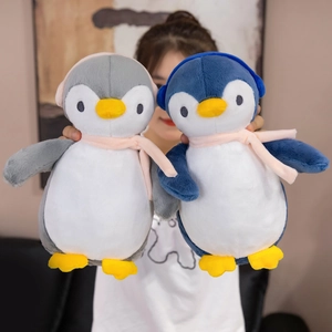 Two cute plush penguins wearing earmuffs and scarves held in hands for size reference