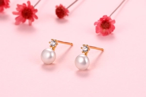 Detailed macro view of white freshwater pearl earrings with gold pins and shiny zircons