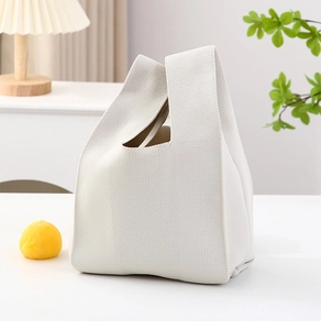 Detailed view of cream knit handbag with textured weave pattern on a minimalist table