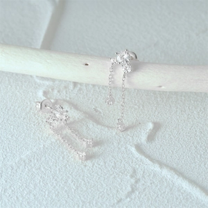 Macro detail of S925 silver tassel earrings with clear gemstones on a natural wood stand