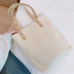 Detailed texture of off-white corduroy tote bag with brown faux leather handles and rivets