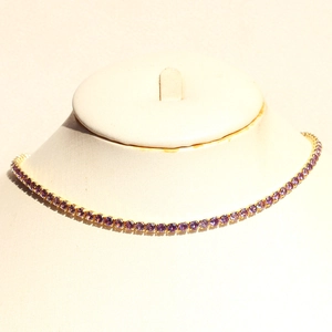 Detail of gold-plated tennis necklace with round-cut purple zirconias on a neck model