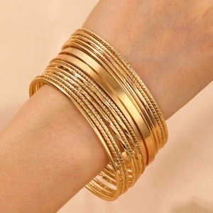 Macro shot of gold-plated bangle set featuring smooth wide bands and textured twist cuffs