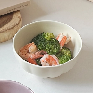 Detail view of a matte light beige ceramic bowl featuring an organic irregular shape