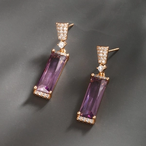 Détail de boucles d'oreilles géométriques avec pierre violette et serti pavé or rose