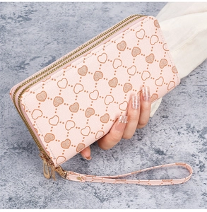 Detail of pink long wallet with heart pattern, dual zippers and wrist strap