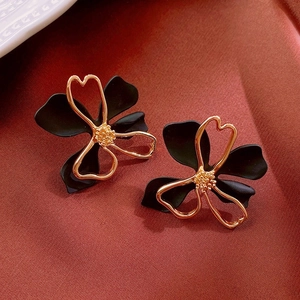 Detailed view of elegant black floral stud earrings with gold metal accents on fabric
