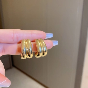 Detail view of thick gold-plated C-shaped earrings with parallel tube design and polished finish