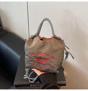 Detailed embroidery of red bows and cherries on brown drawstring nylon bucket bag