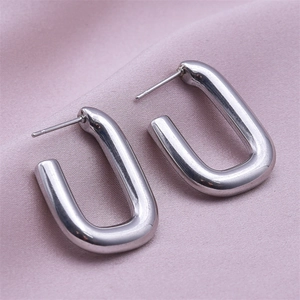 Macro view of silver U-shaped stainless steel earrings on soft pink silk background