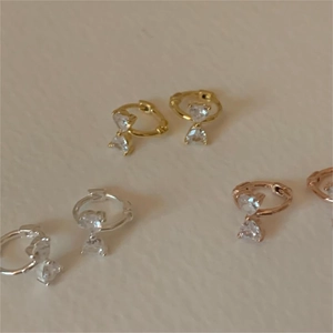 Close-up of bow knot earrings with double heart-shaped zircons in gold, silver, and rose gold