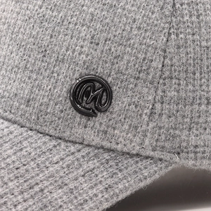 Detailed macro view of the grey knit texture and round metal M logo on the baseball cap