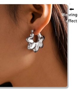 Close-up of silver irregular wavy hoop earring worn on ear with high metallic luster