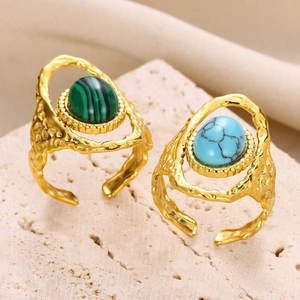 Détail de deux bagues dorées avec pierres turquoise ovales vertes et bleues sur un rocher
