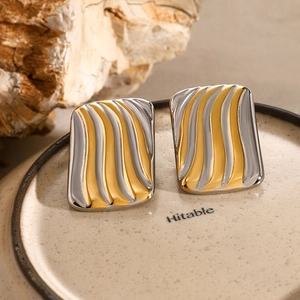 Detail of two-tone gold and silver rectangular earrings with wave texture on ceramic tray