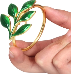 Detailed view of a gold napkin ring with green leaf design held by a hand on white background