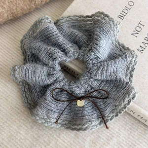 Close-up of grey knitted scrunchie with a brown bow and gold tag on a book