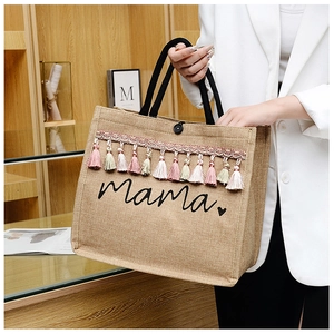 Detail of linen tote bag featuring fringe tassels and embroidered mama script text